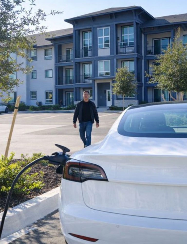 Valkoinen sähköauto latauksessa taloyhtiön parkkipaikalla.